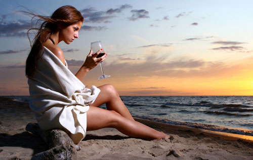 美女坐在夕阳下的沙滩上优雅品酒