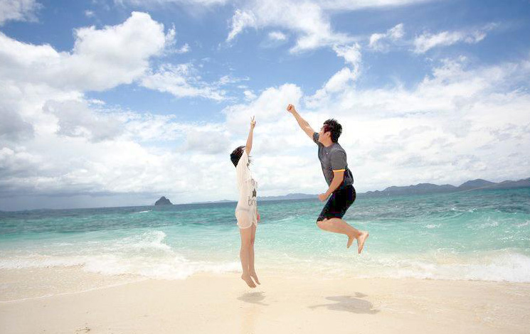 情侣在沙滩上跳起来拍美照